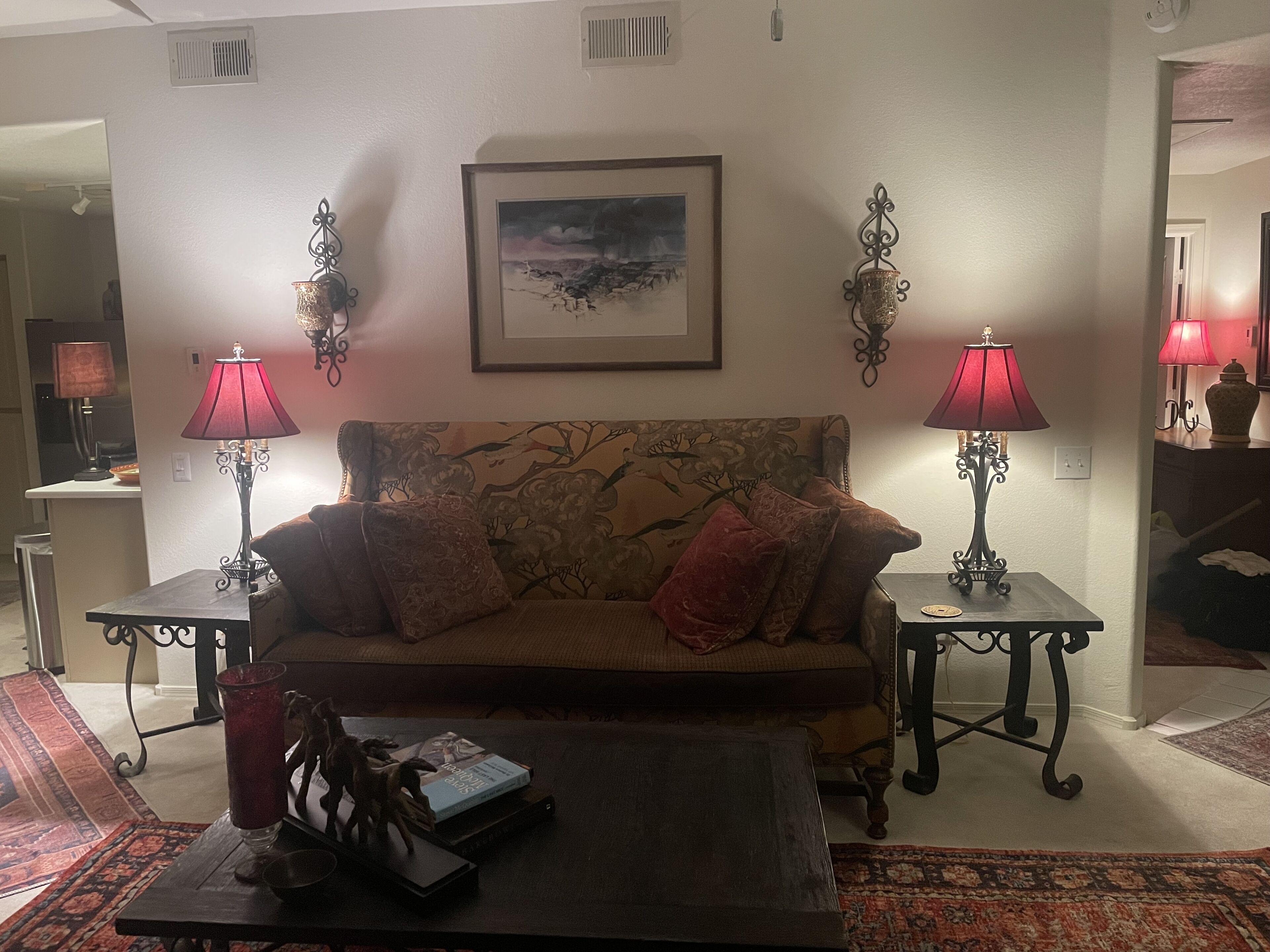 Un salón con un sofá, dos mesitas de noche con lámparas, un cuadro en la pared y una mesa de centro con libros y un objeto decorativo.