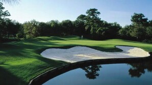 Ein Golfplatz mit einem Sandbunker, einer Wasserfalle und Bäumen im Hintergrund.