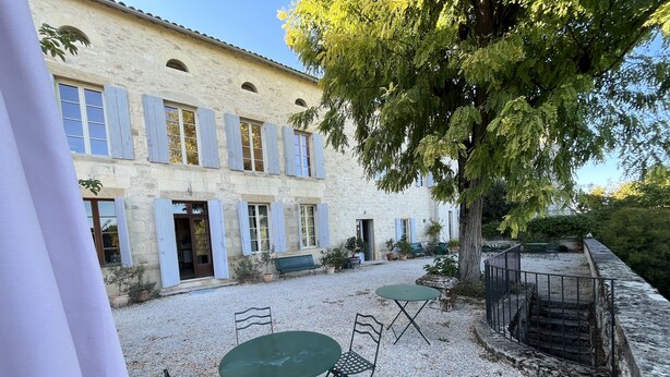 A courtyard with a stone building, outdoor seating, and a tree.