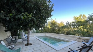 A pool area with lounge chairs and a tree.