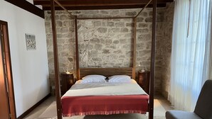 A four-poster bed with a wooden headboard, two bedside tables with lamps, a red bedspread, and a grey chair.