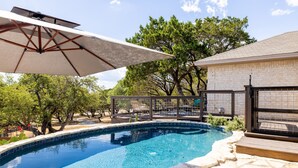 Una piscina con borde de piedra, rodeada por una terraza de madera y un área cubierta con sillas.