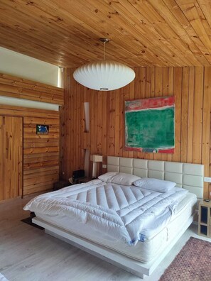 A bedroom with wooden paneling, a large bed with white bedding, a ceiling fan, and a green abstract painting on the wall.