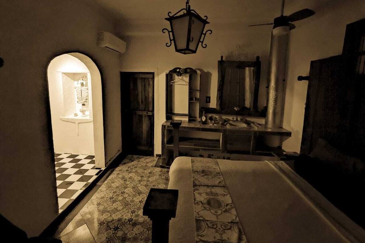 A dimly lit room with a checkered floor, a bed, a dresser, and a mirror.