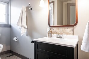 Une salle de bain avec un lavabo blanc, des meubles sombres, un miroir et une serviette accrochée au mur.