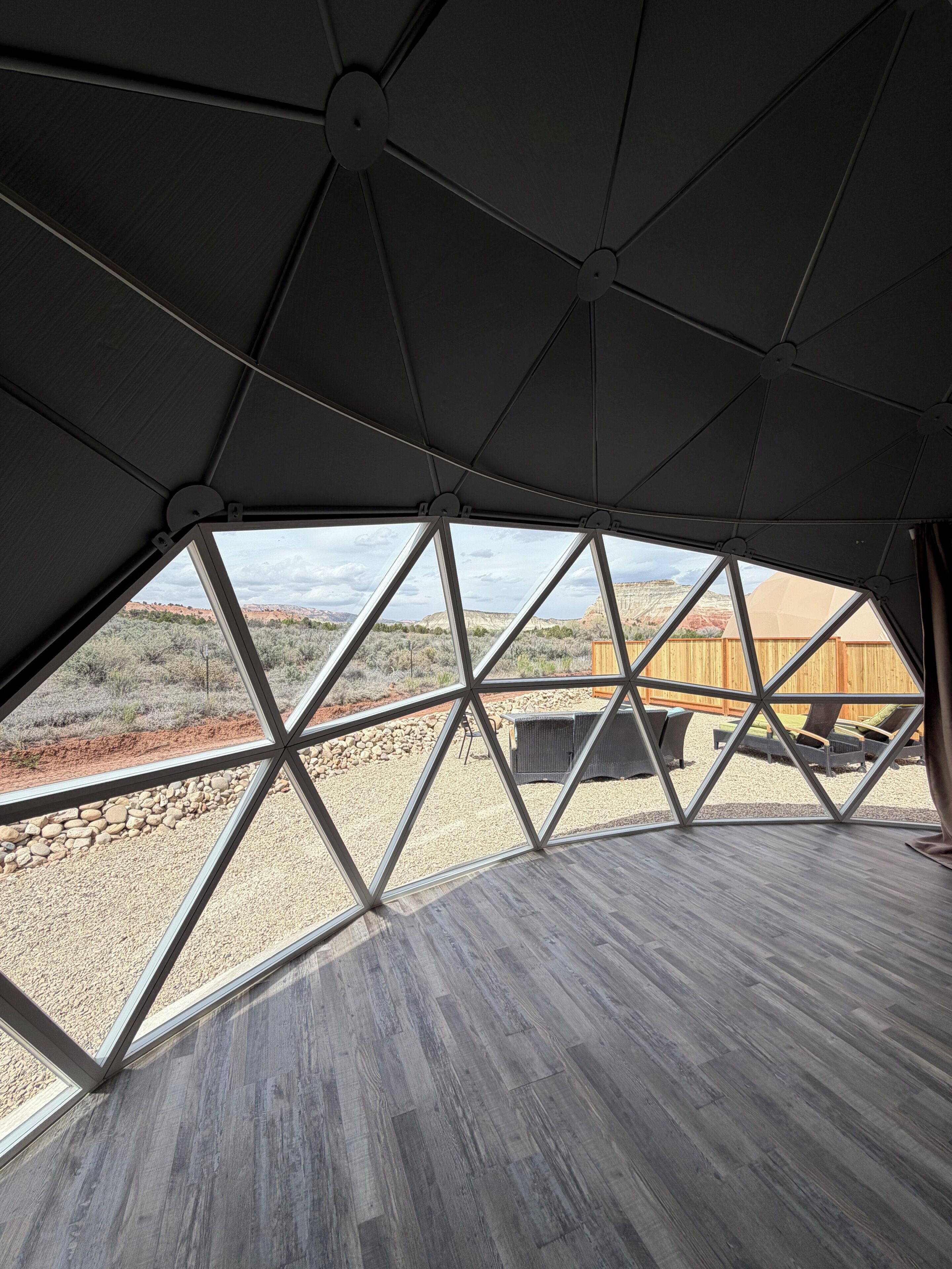 A room with a geometric ceiling design, a view of a desert landscape, and a wooden floor.