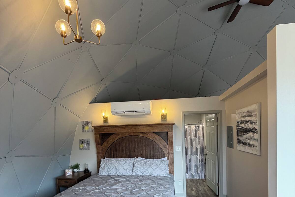 Une chambre avec un lit en bois, un ventilateur de plafond et un luminaire moderne.