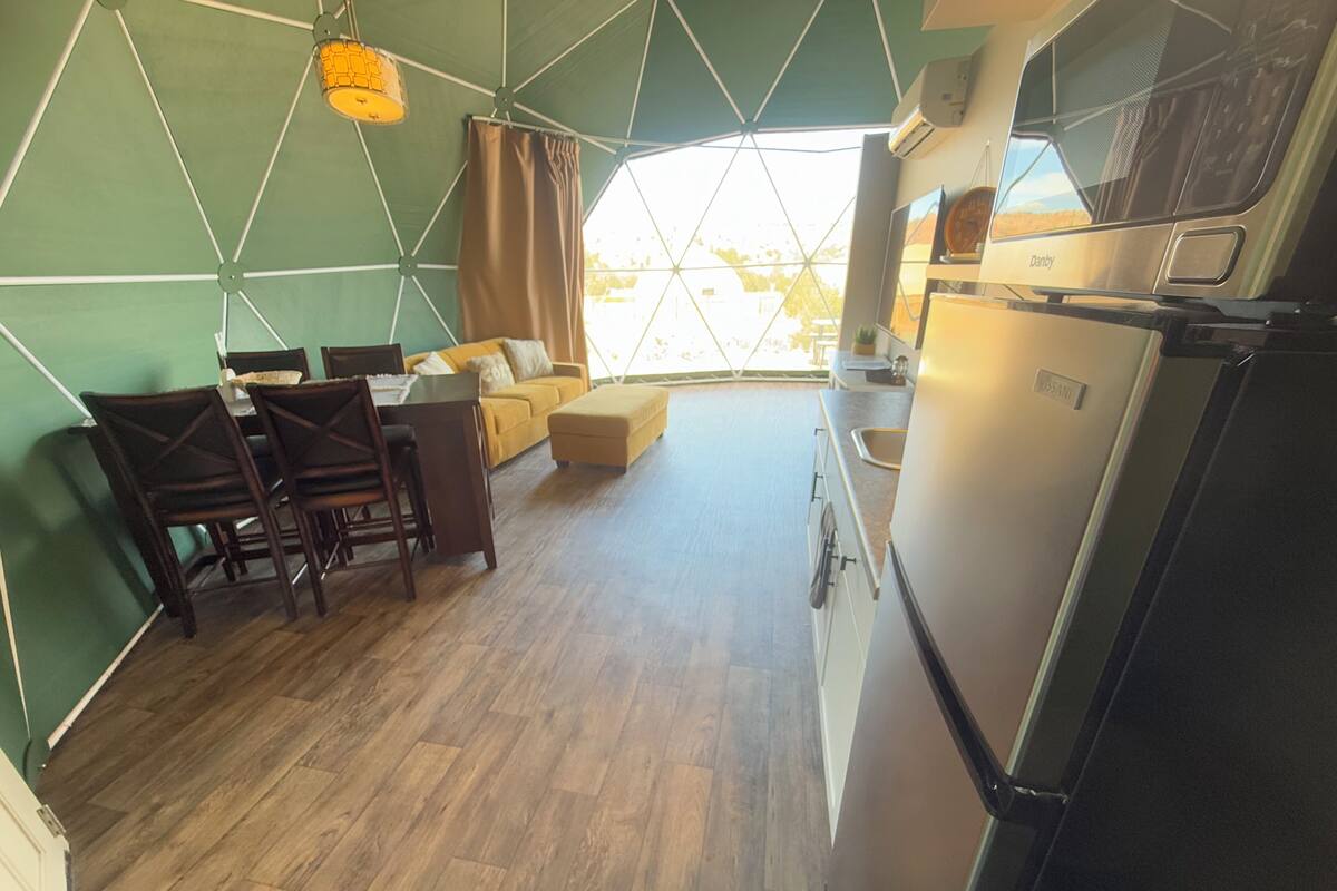 Un espace de vie compact comprenant un coin repas, une kitchenette et une grande fenêtre laissant entrer la lumière naturelle.