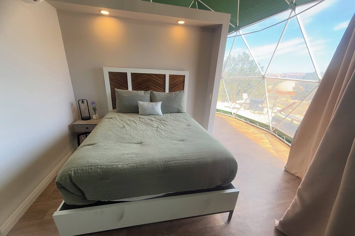 Une chambre à coucher moderne, dotée d’un grand lit, d’une table de chevet et offrant une vue sur l’extérieur grâce à une grande fenêtre.