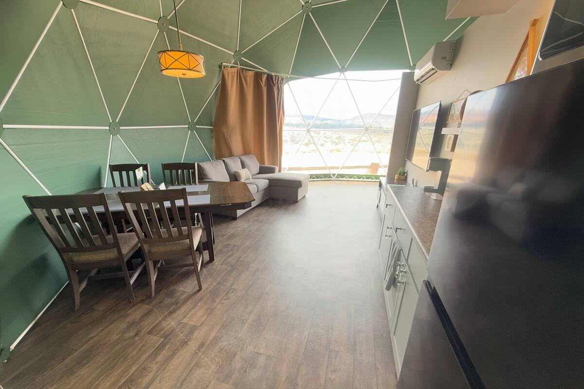 Une cuisine moderne avec un grand réfrigérateur, une table à manger en bois avec des chaises, un canapé et un luminaire suspendu.