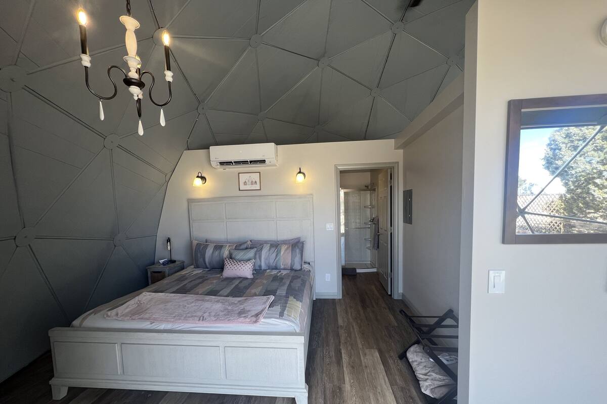 Une chambre à coucher avec un grand lit, un lustre, un appareil de climatisation et une vue sur l’extérieur par une fenêtre.