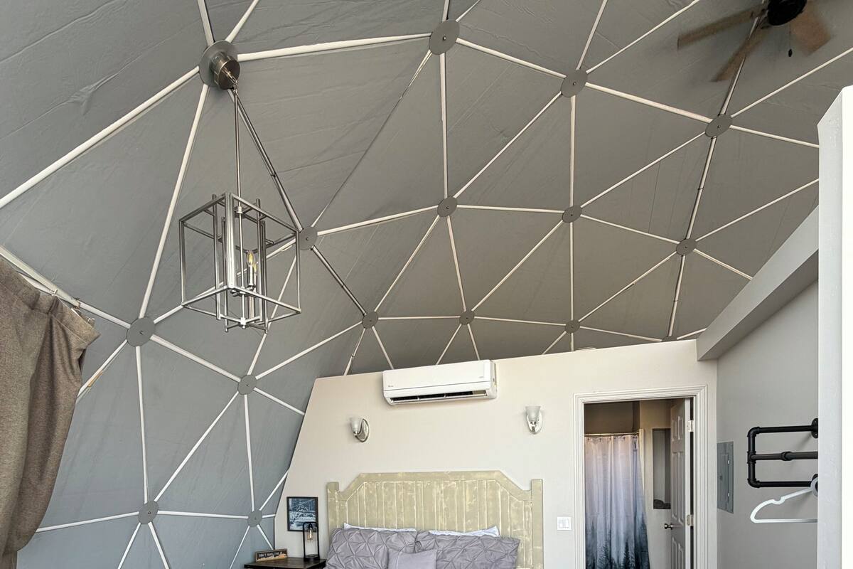 Une chambre à coucher avec un plafond aux motifs géométriques, un lit, une table de chevet, un luminaire suspendu et un appareil de climatisation.