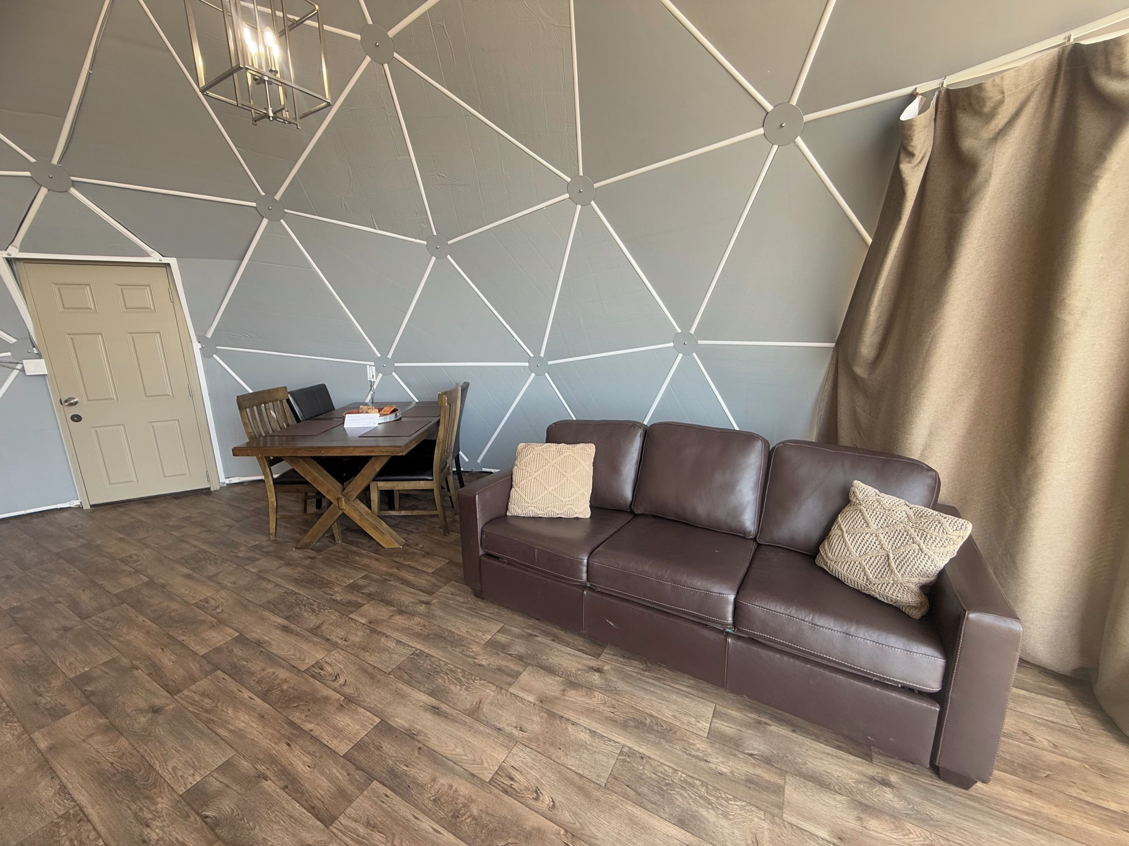 A room with a brown leather sofa, a wooden dining table with chairs, and a geometric-patterned wall.