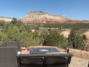 Un set di sedia e tavolino in vimini su un patio con vista su un paesaggio montuoso e cielo sereno.