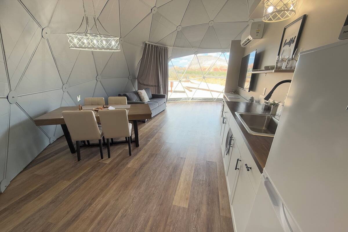 Une cuisine moderne avec un coin repas, caractérisée par un plafond au design géométrique, un plancher en bois et une vue sur l’extérieur.