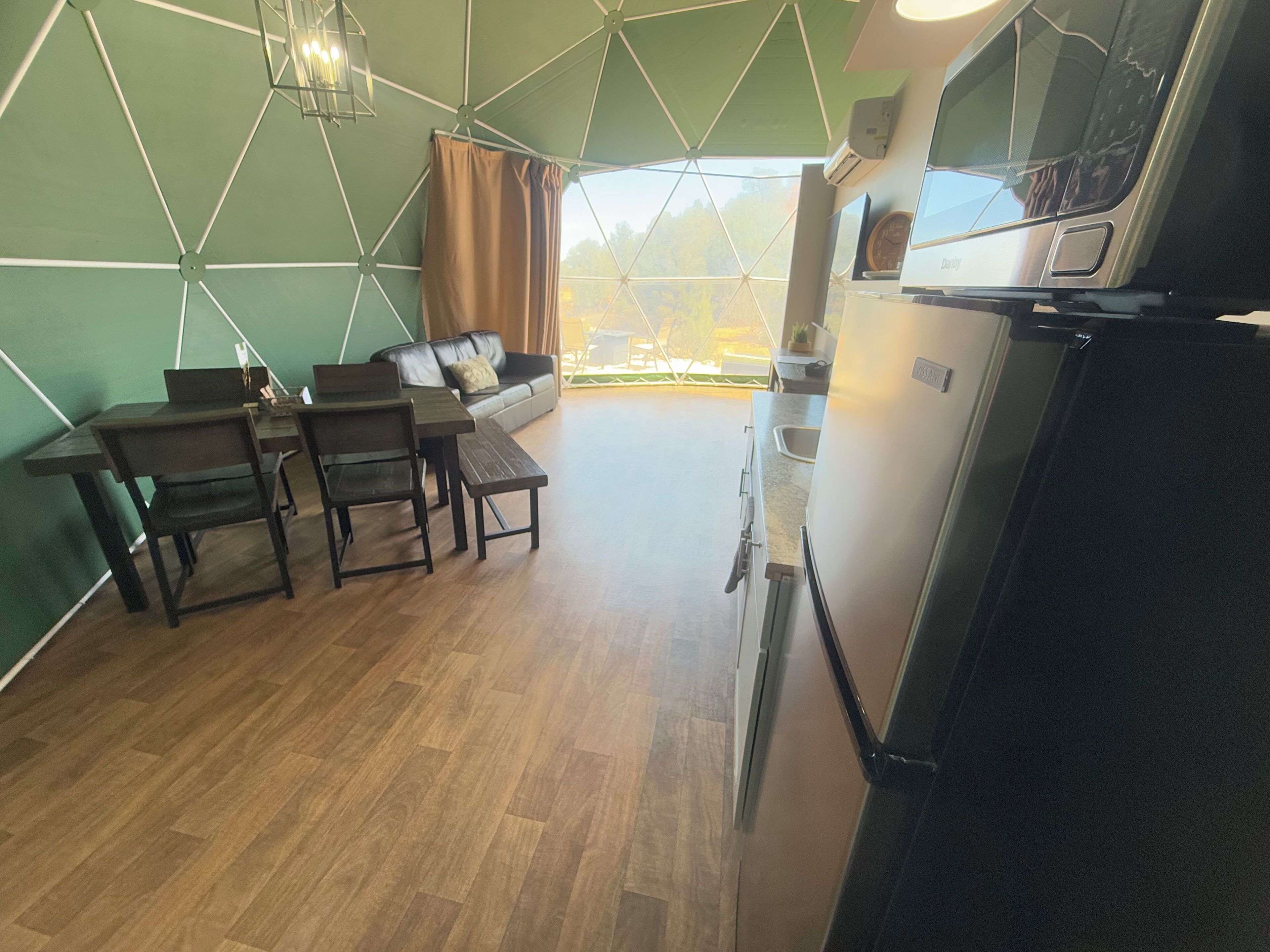 A modern living room with a dining area, kitchen, and large windows offering a view of the outdoors.
