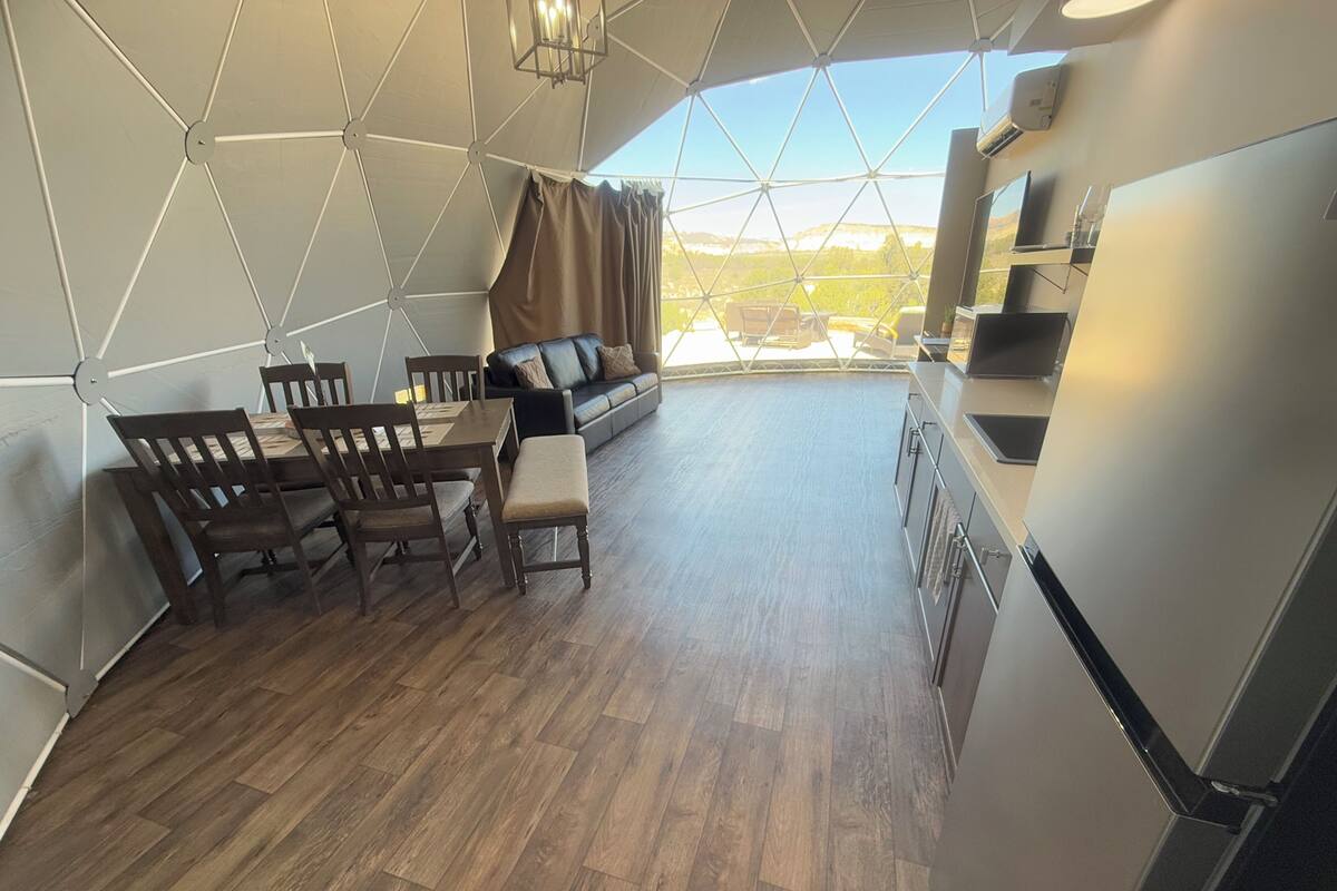 Une cuisine moderne avec un coin repas, comprenant une table et des chaises en bois, un canapé et une grande fenêtre donnant sur l’extérieur.