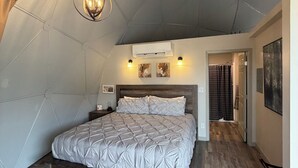 Een slaapkamer met een houten bedframe, een plafondventilator, een airconditioningsysteem en een hal die naar een badkamer leidt.