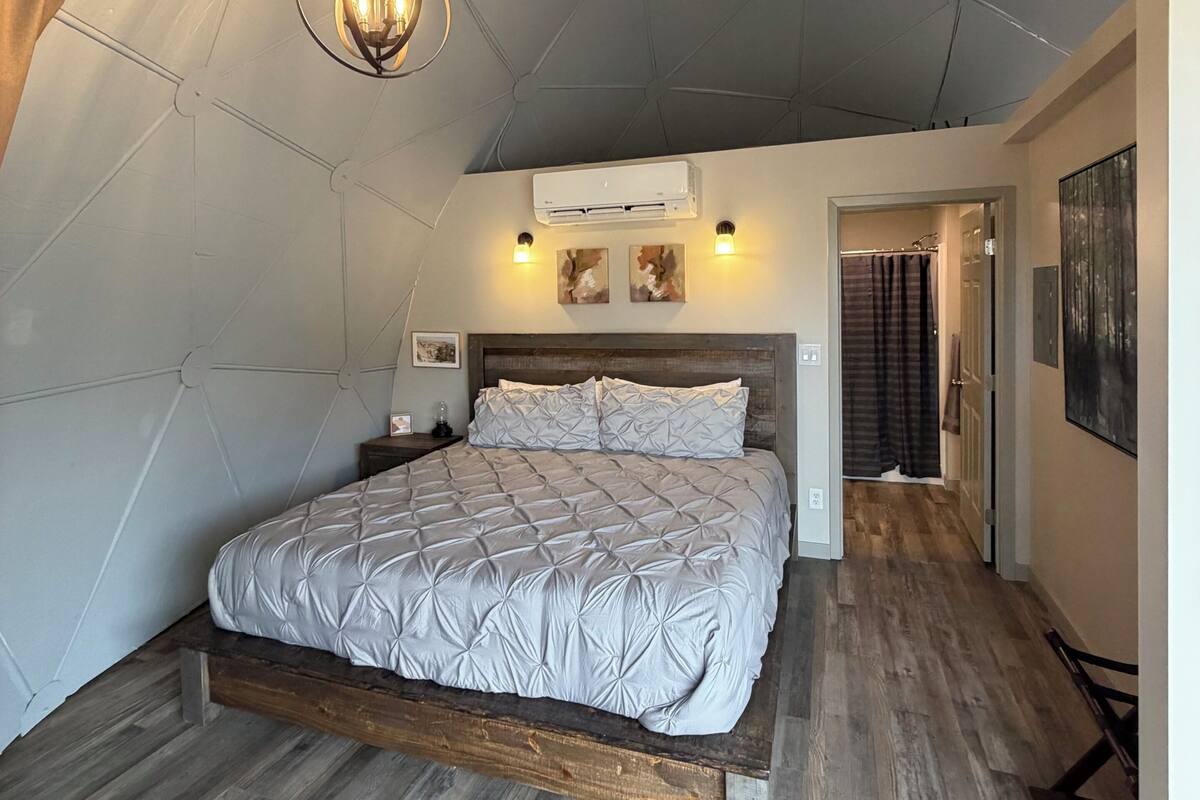 Une chambre avec un lit en bois, un ventilateur de plafond, un appareil de climatisation et un couloir menant à une salle de bain.