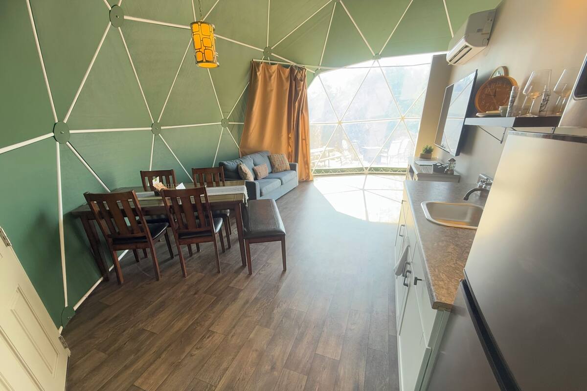 Une cuisine moderne avec un évier, un coin repas avec des chaises en bois, un canapé et une grande fenêtre avec des rideaux.