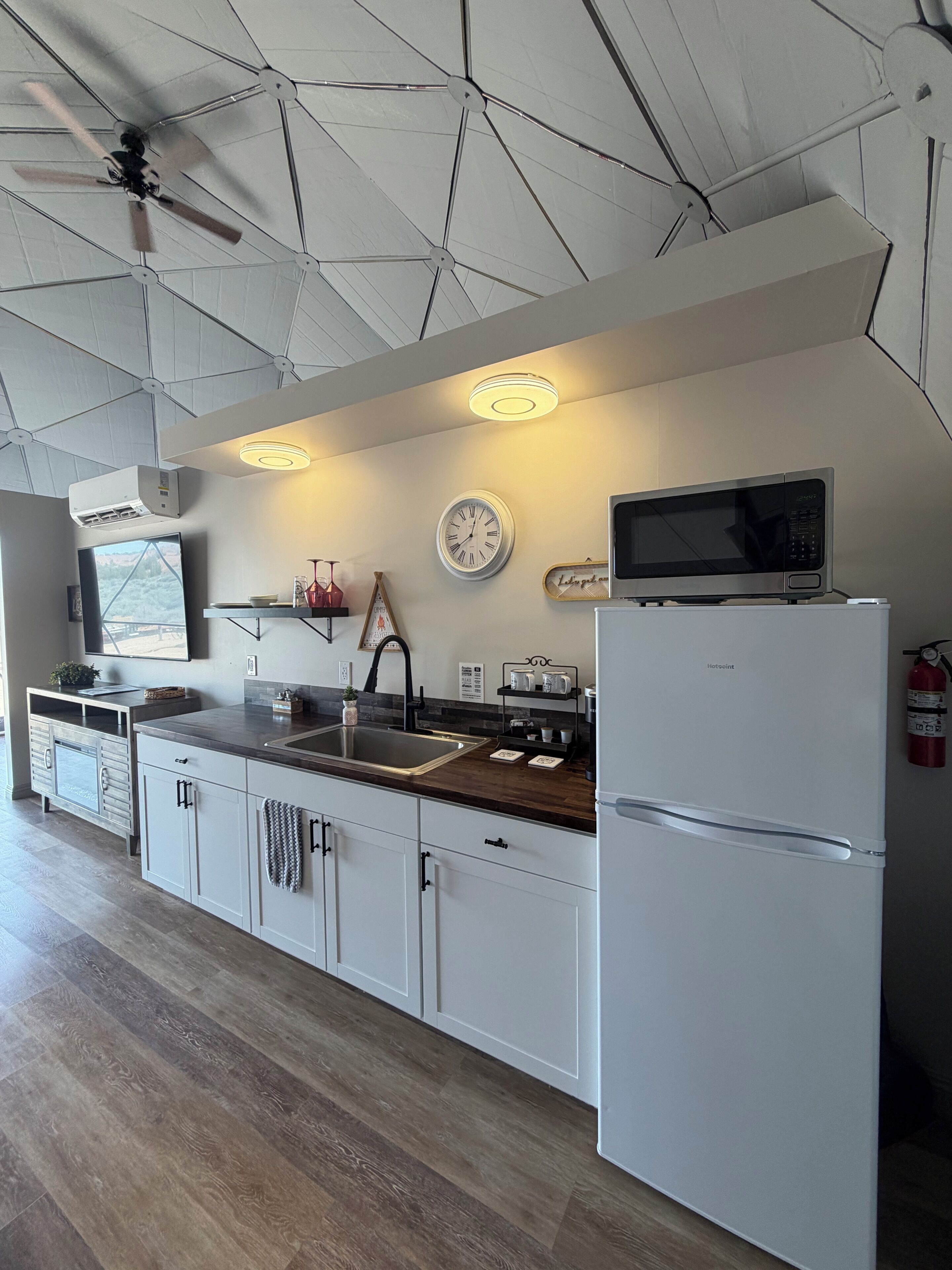 A modern kitchen with white cabinetry, a stainless steel sink, a microwave, and a ceiling fan.