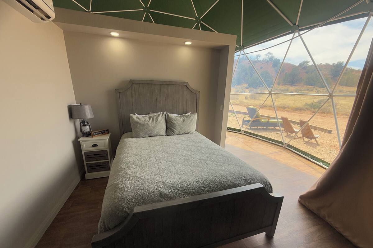 Une chambre à coucher avec un grand lit, une table de chevet, une lampe et une vue sur l’extérieur grâce à une grande fenêtre.