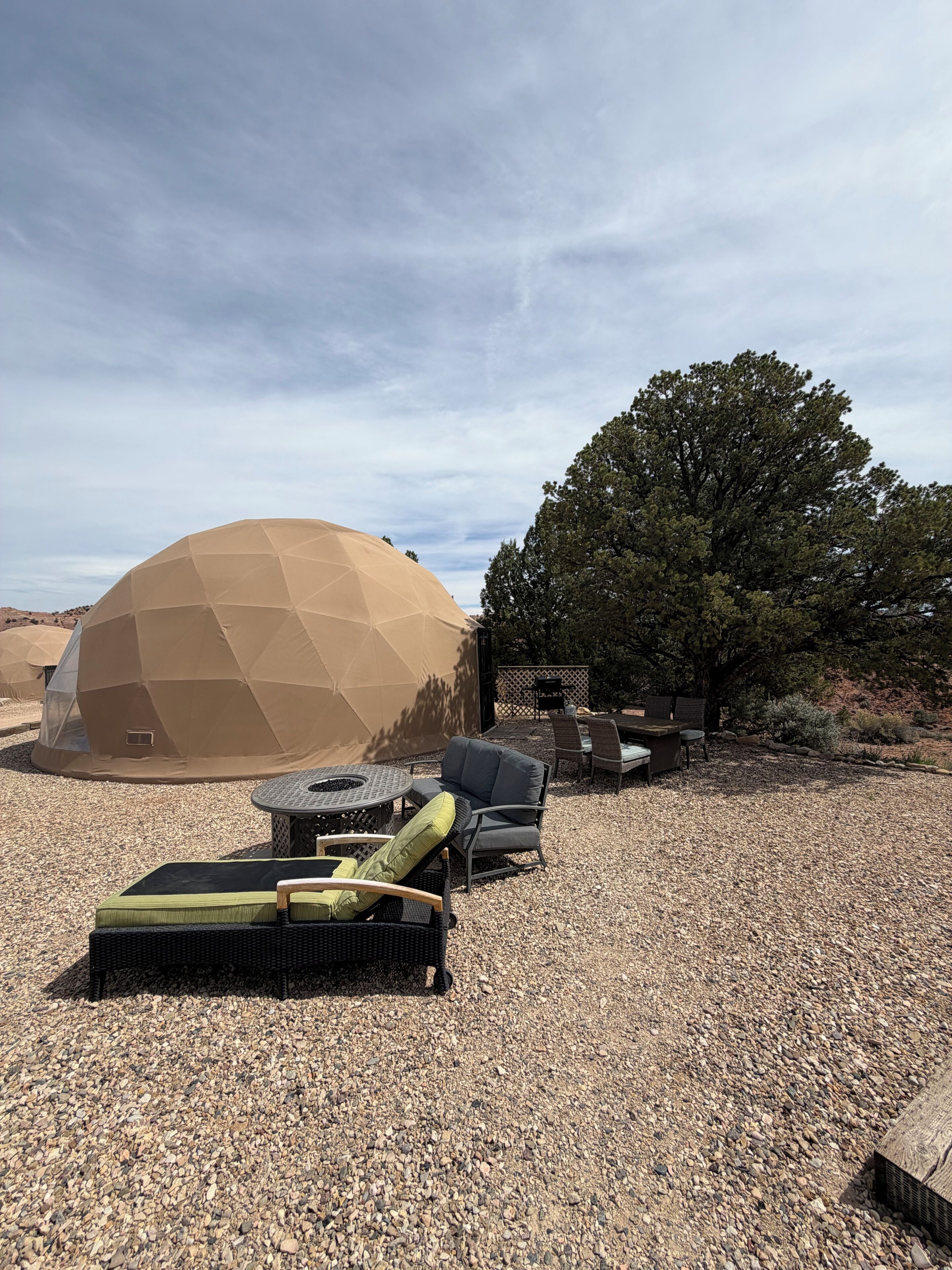 A geodesic dome structure, outdoor seating area with chairs and a table, and a large tree.
