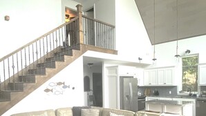 A spacious living room with a large L-shaped sectional sofa, a staircase leading to an upper level, and a modern kitchen in the background. - Gorgeous lake house with sandy beachfront. Welcome to Lost  World Landing  (Eufaula)