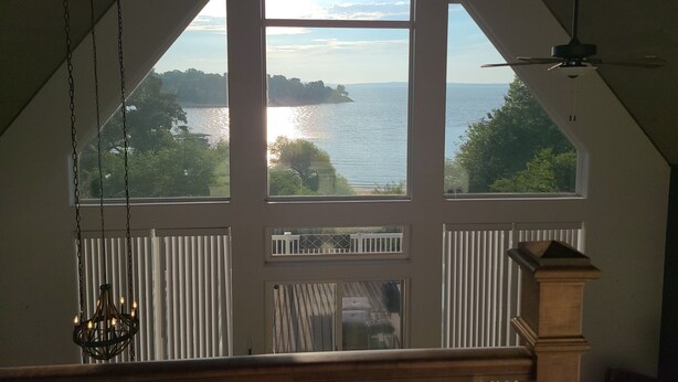A room with a large bay window overlooking a body of water, a chandelier, and a ceiling fan. - Gorgeous lake house with sandy beachfront. Welcome to Lost  World Landing  (Eufaula)