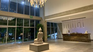 Een moderne lobby met een grote Boeddha-beeld, een receptiebalie en een kroonluchter.