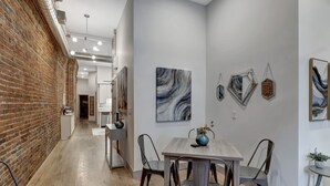 Ein modernes Interieur mit freiliegenden Backsteinwänden, Holzdielen und einer Essecke mit Tisch und Stühlen.