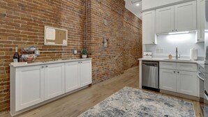 Una cucina con mobili bianchi, un muro in mattoni, pavimento in legno e un tappeto.