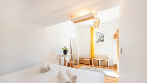 Ein modernes Schlafzimmer mit einem großen Bett, einem kleinen Tisch mit einer Pflanze, einer Bank und Blick ins Freie.