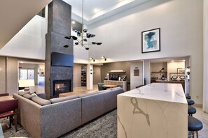 A modern living room with a fireplace, a large sofa, a dining area, and a kitchen in the background. - 1 Bedroom | Free Breakfast + Outdoor Pool (Albuquerque)