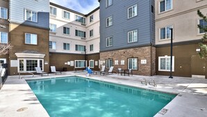 A swimming pool with lounge chairs, a covered area, and a building with multiple windows and a door.