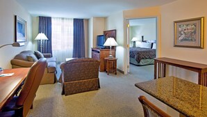 A hotel room with a desk, two chairs, a sofa, a television, a lamp, and a bed.