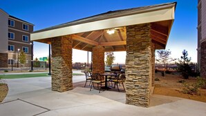 A covered patio with stone pillars, outdoor furniture, and a grill area.