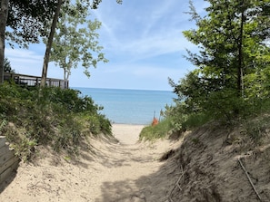 A sandy path leading to a beach with a wooden fence on one side and trees on the other.
