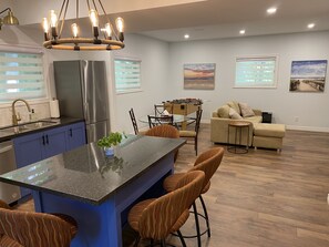 Uma cozinha moderna com uma ilha central, uma sala de jantar com mesa de pebolim e uma sala de estar com sofá e mesa de centro.