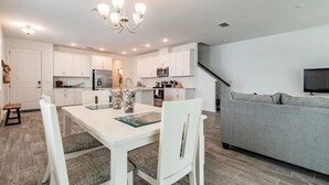Una cocina moderna con armarios blancos, una mesa de comedor con sillas y un sofá gris en la sala de estar.