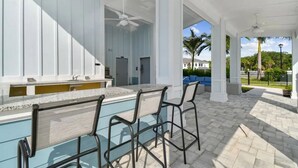 Una cocina exterior moderna con barra, columnas blancas y vistas del paisaje circundante.