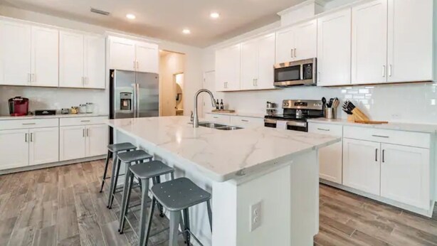 Una cocina moderna con armarios blancos, una isla grande con taburetes de bar, electrodomésticos de acero inoxidable y piso de madera.