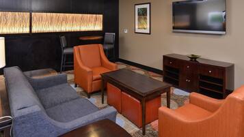 A modern living room with a sofa, armchairs, a coffee table, and a flat-screen TV mounted on the wall.