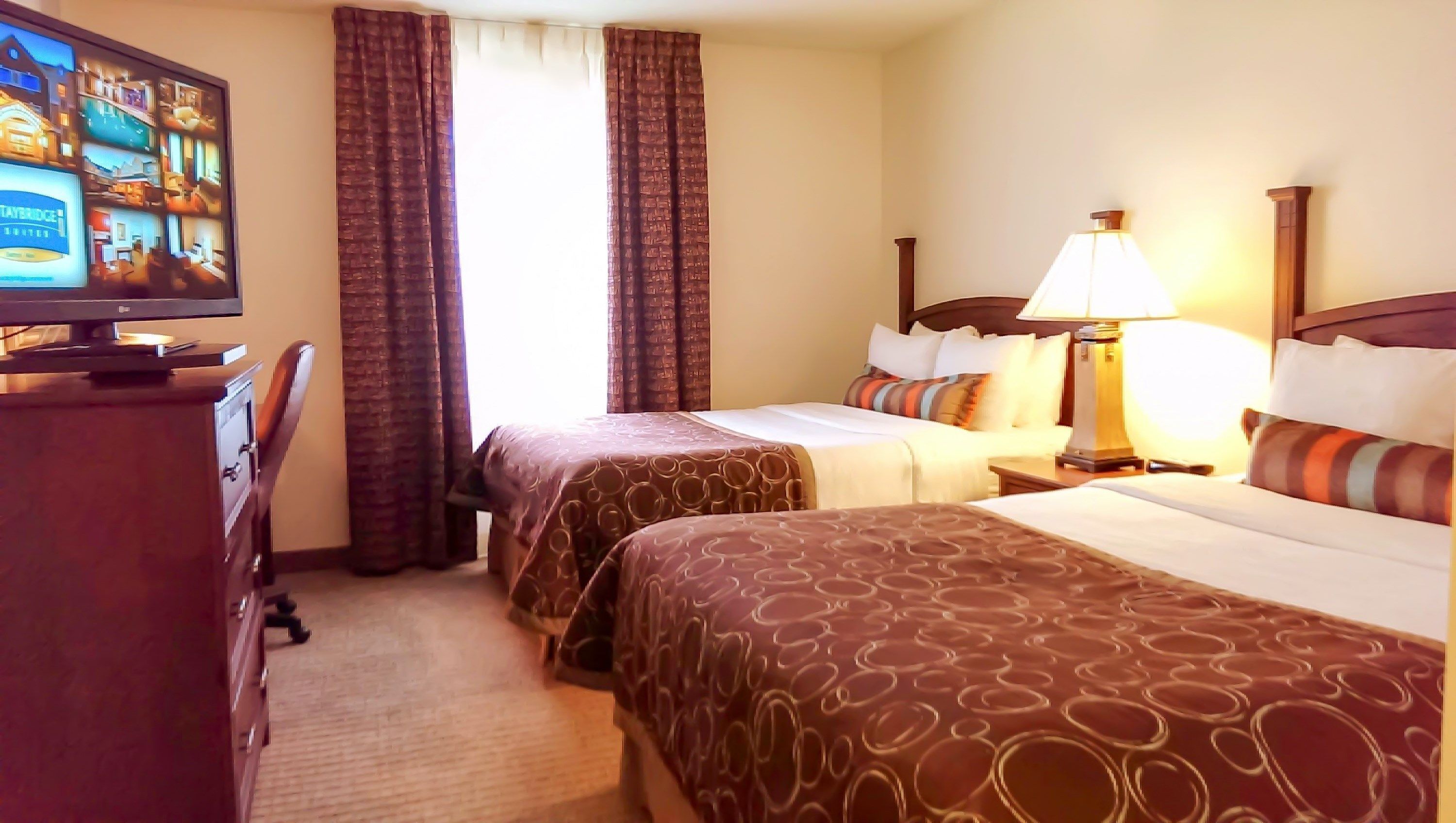 A hotel room with two beds, a TV, a desk, and a lamp.