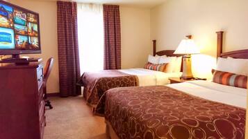 A hotel room with two beds, a TV, a desk, and a lamp.