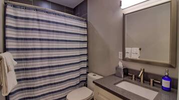 A bathroom with a striped shower curtain, a toilet, a sink with a mirror, and a blue bottle on the counter.
