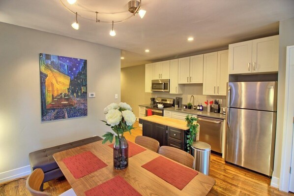 A modern kitchen with white cabinets, stainless steel appliances, and a dining area with a wooden table and red placemats.