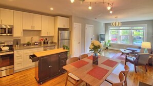 A modern kitchen with stainless steel appliances, a central island, and a dining area with a table and chairs. - Stunning Minimalist Gem | Fenced Backyard + W/D (Saint Louis)