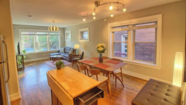 A spacious living area with a dining table, sofa, and a large window with blinds. - Stunning Minimalist Gem | Fenced Backyard + W/D (Saint Louis)