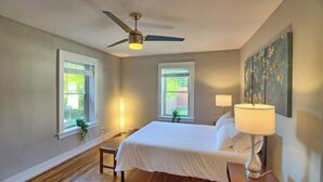A bedroom with a bed, bedside lamps, a ceiling fan, and two windows. - Stunning Minimalist Gem | Fenced Backyard + W/D (Saint Louis)